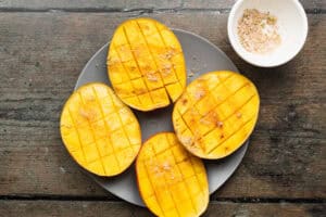 Grilled mango with chili-lime salt and fresh lime juice on a plate on a wooden table.