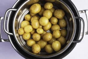 Overhead view of raw petite potatoes in a steamer basket resting in a large pot.