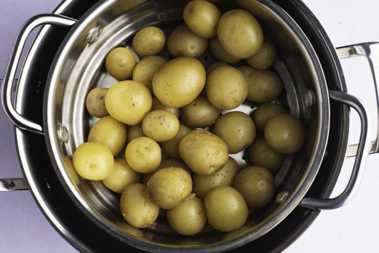 Overhead view of steamed potatoes in a steamer basket sitting in large pot.