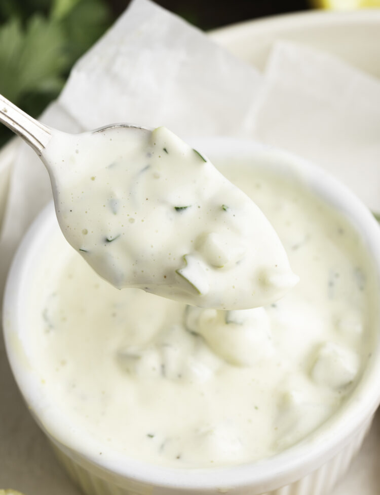 Vegan tartar sauce being lifted out of a small white ramekin on a silver spoon.