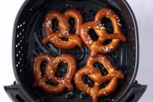 Overhead view of 4 twisted, salted, frozen soft pretzels in the air fryer basket.