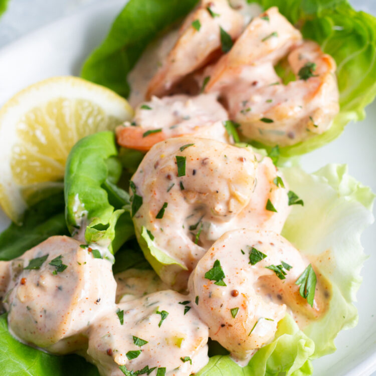 Close-up view of shrimp remoulade on a bed of lettuce with lemon wedges.