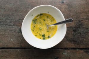 Overhead view of garlic-butter sauce in a small white bowl with a fork.