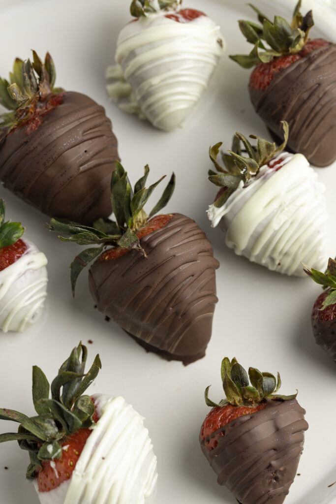 Close up photo of dark chocolate and white chocolate covered strawberries on a white plate.