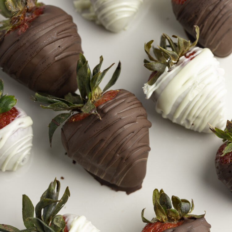 Close up photo of dark chocolate and white chocolate covered strawberries on a white plate.