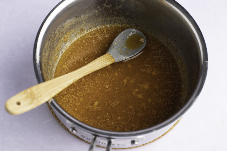 Overhead view of garlic butter sauce in silver saucepan with large spoon.