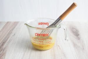 Ingredients for chicken marinade in glass measuring cup with wooden-handled whisk.