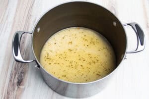 Overhead view of rice with chicken broth in large pot on neutral background.