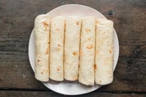 Overhead view of air fryer flautas lined up on a plate before being air fried.