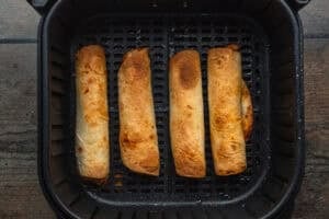 Overhead view of 4 golden brown crispy air fryer flautas in an air fryer basket.