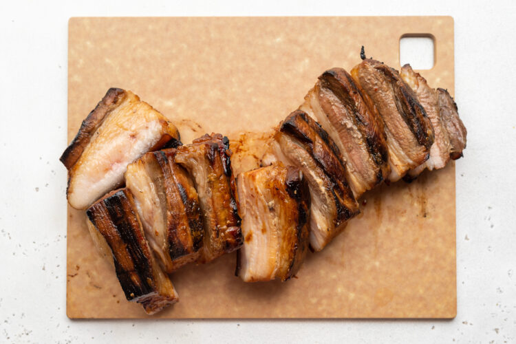 Overhead view of grilled pork belly, sliced and resting on a cutting board.