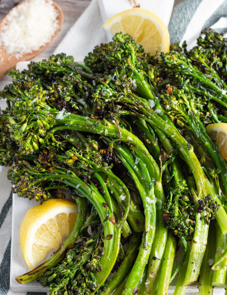 Overhead view of grilled broccolini on a platter with lemon wedges.