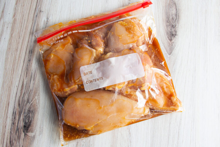 Overhead view of boneless, skinless chicken thighs in plastic freezer bag with mesquite marinade.