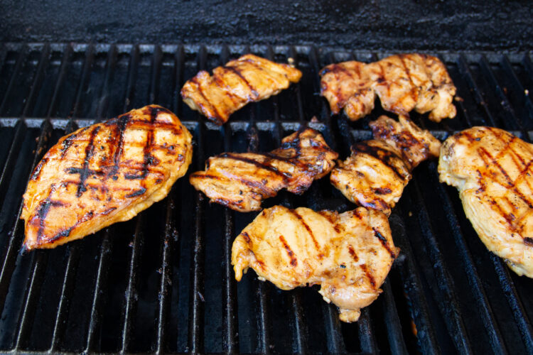 Mesquite grilled chicken thighs on grill grates with char marks on top of chicken.