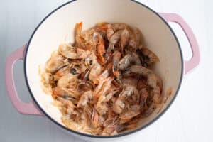 Overhead view of shrimp shells and avocado oil in a large dutch oven on a neutral background.