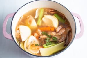 Overhead view of shrimp stock ingredients and water in large dutch oven on neutral background.