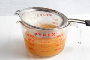Sieve resting in glass measuring cup containing strained shrimp stock without aromatics.