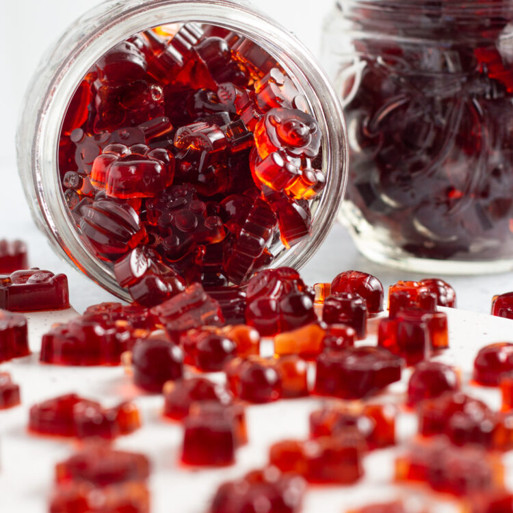Side view of a jar of tart cherry gummies, with cherry gummies spilling out onto a white countertop.