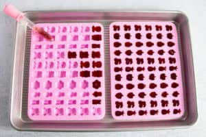 Overhead view of two gummy molds partially filled with tart cherry gummy liquid, with a dropper of liquid on one mold.