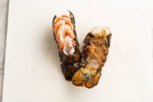 Overhead view of two lobster tails on a cutting board, with one flipped over to show ribs underneath tail.