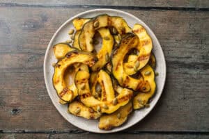 Overhead view of grilled acorn squash slices pilled on a white plate on a wooden countertop.