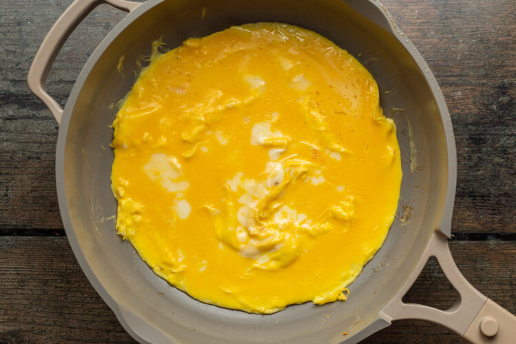 Overhead view of scrambled eggs spread out across a hot skillet to create a Mexican omelette.