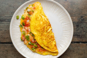 Overhead view of Mexican omelette, folded in half and resting on a white plate on a wooden table.