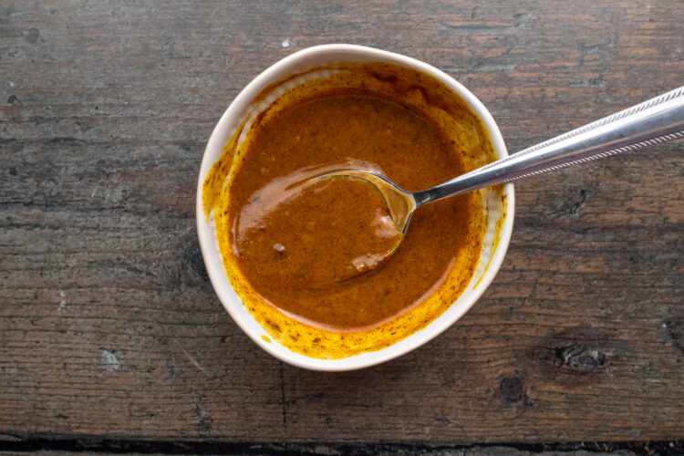 Overhead view of smoky mustard sauce in a small white bowl with a silver spoon.