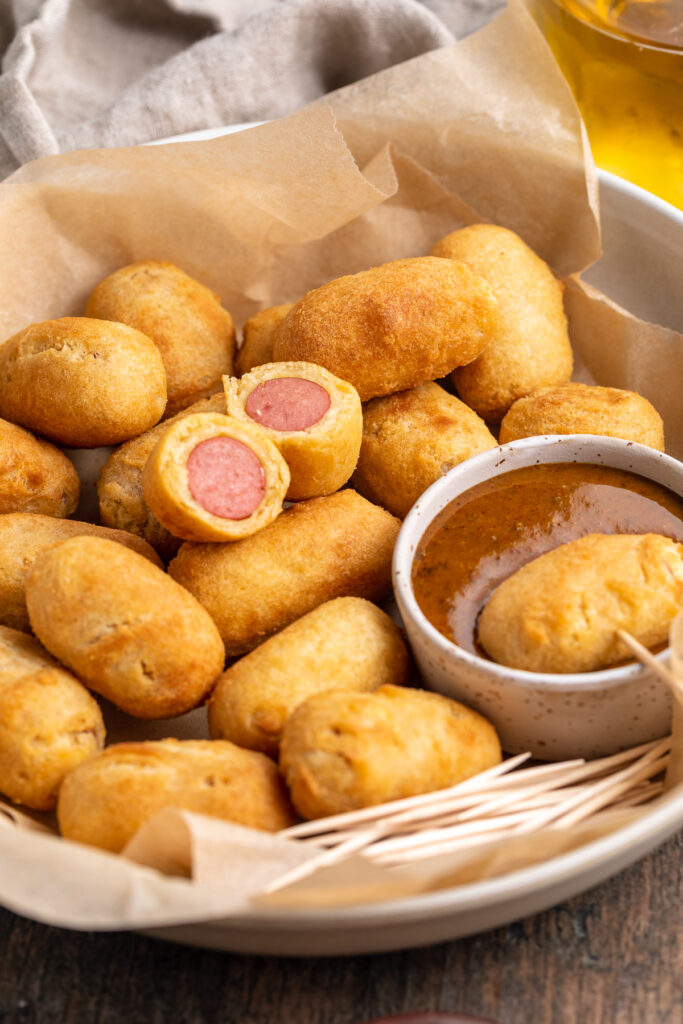 Overhead, angled view of mini corn dogs cooked in the ai fryer on a platter with a smoky mustard dipping sauce.