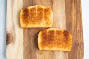 Two slices of toasted bread on a wooden cutting board.