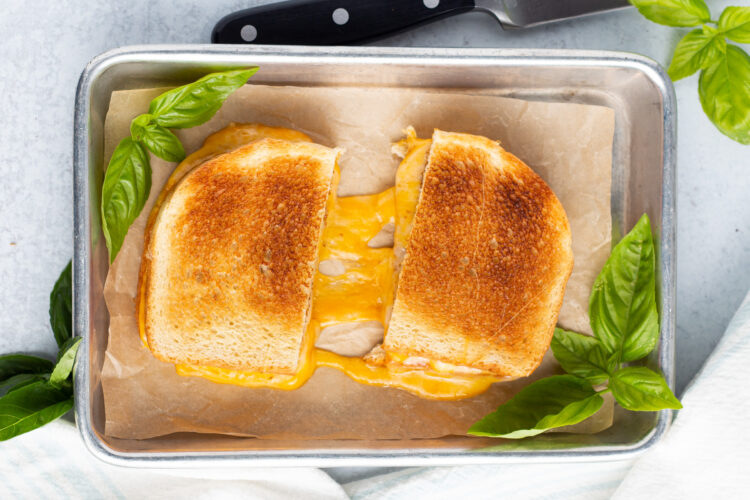 Overhead view of a toasted grilled cheese sandwich on a baking sheet. Sandwich is cut in half to show cheese pull.