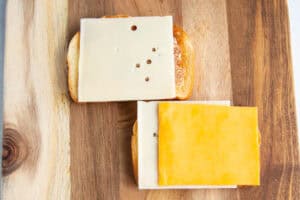 Overhead view of two slices of buttered toast topped with 3 slices of cheese on a wooden cutting board.