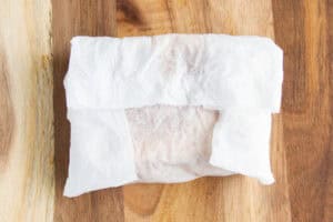 Overhead view of a toasted grilled cheese sandwich wrapped in a damp paper towel on a wooden cutting board.