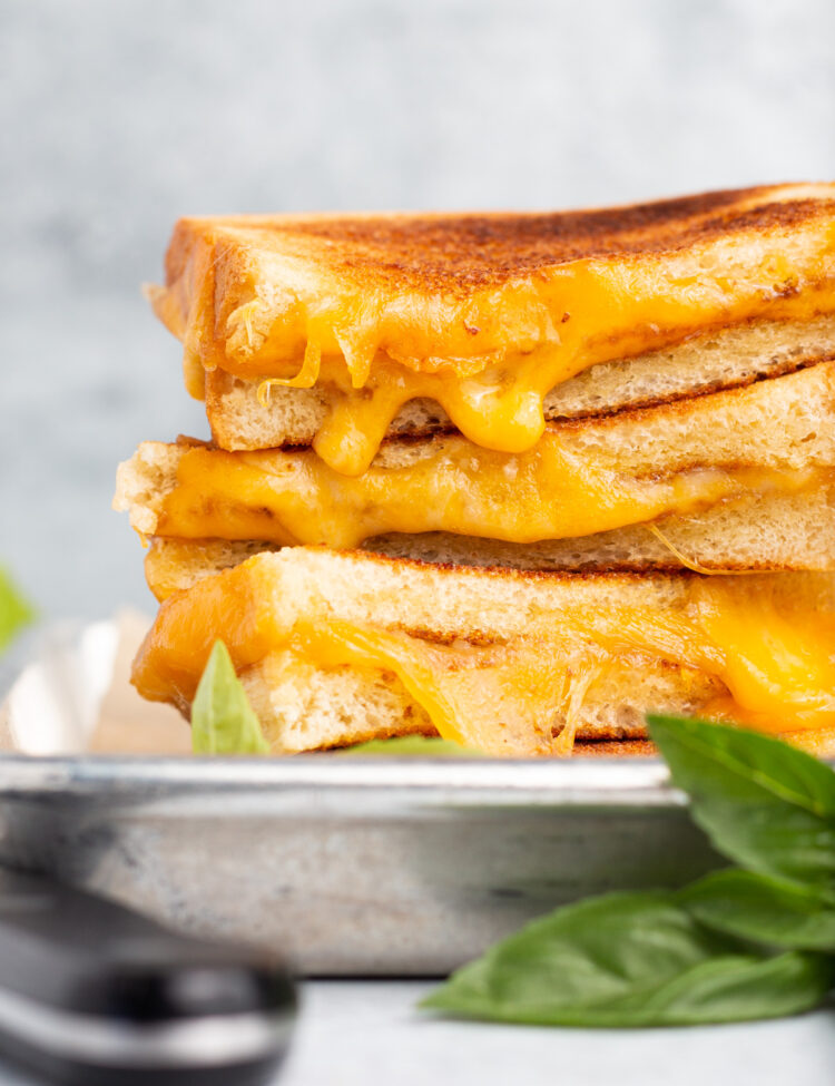 Side view of 4 toasted grilled cheese halves stacked on top of eachother with cheese oozing out toward the camera.
