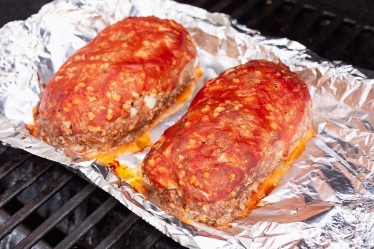 Angled view of two uncooked meatloaves on aluminum foil on a grill grate.