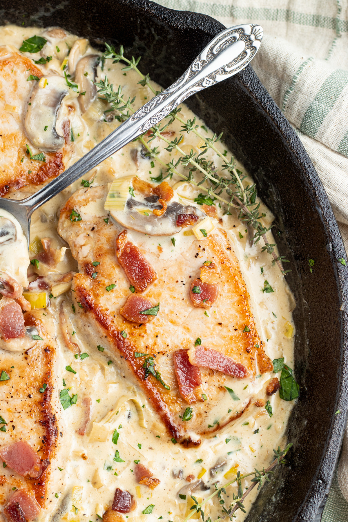 Overhead, close-up look at keto smothered pork chops in a large cast iron skillet with a creamy sauce.