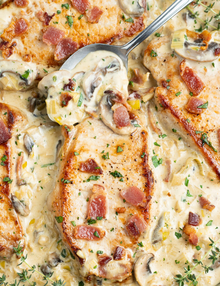 Close-up look at keto smothered pork chops in a large cast iron skillet with a creamy sauce.