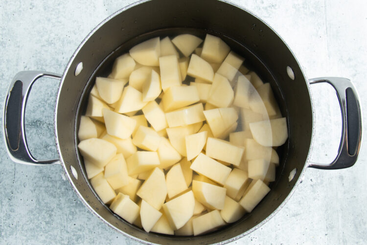 Overhead view of cubed potatoes in a pot with two handles on a white countertop.