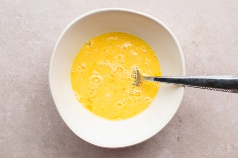 Overhead view of eggs and milk mixed together in a white bowl until egg mixture is pale yellow.