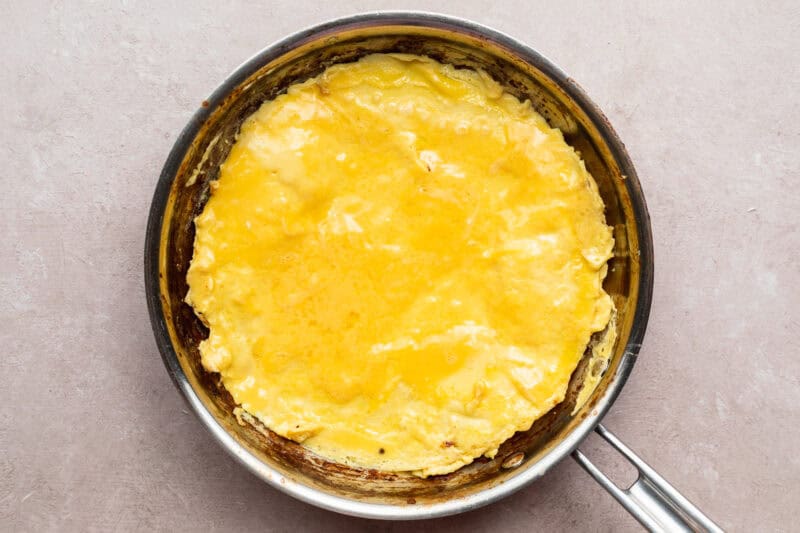 Overhead view of firm, cooked eggs in a large silver skillet on a neutral countertop.