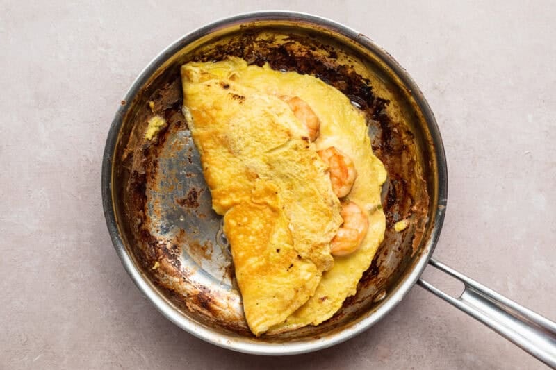 Overhead view of a folded shrimp omelette with green onions and eggs in a large silver skillet.
