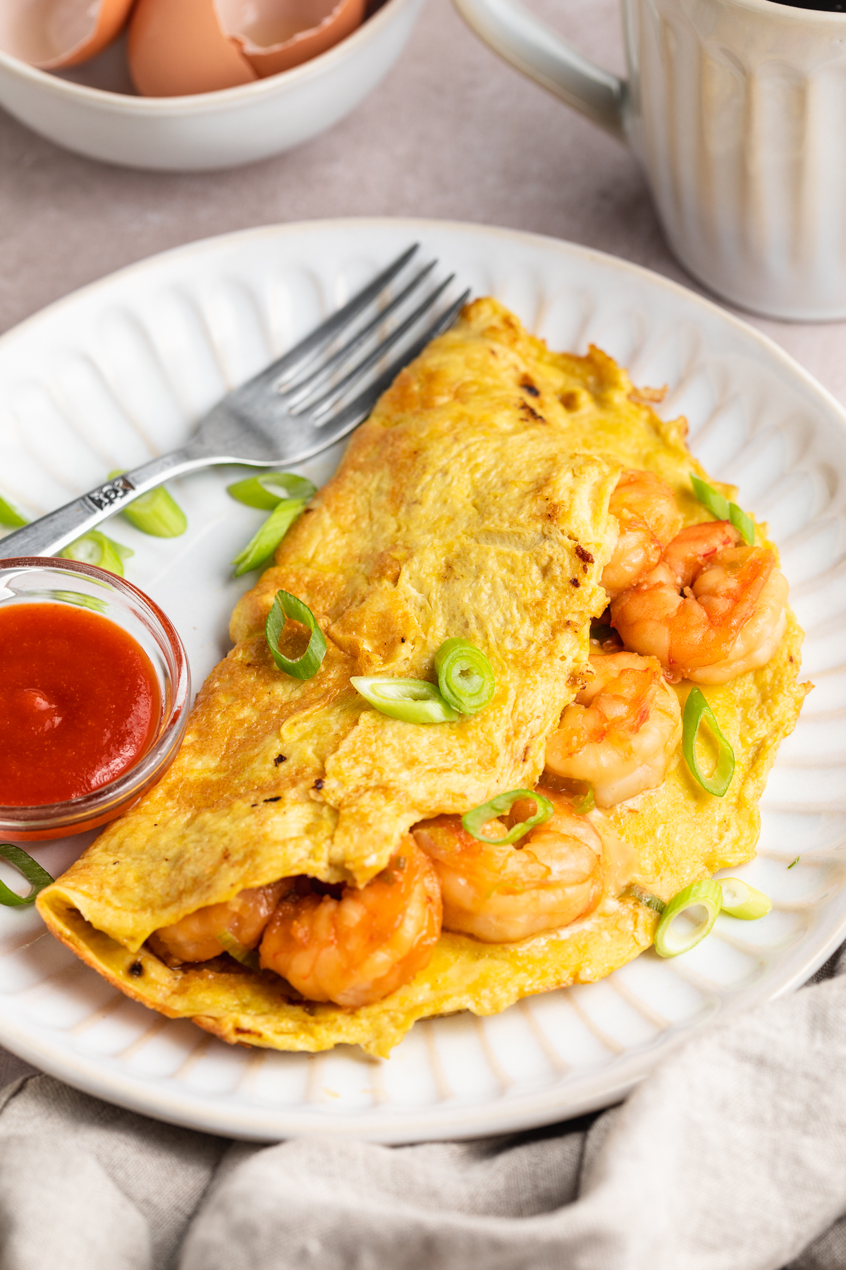 3/4-angle view of a folded omelette stuffed full with tender shrimp on a white plate next to a small bowl of ketchup.
