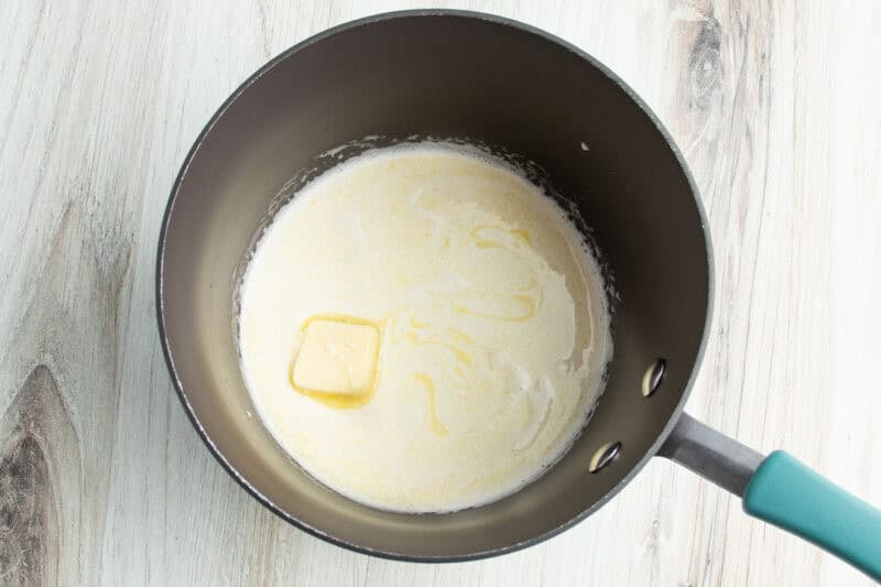 Overhead view of melting butter and heavy cream in a small saucepan on a white countertop.