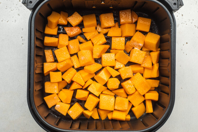 Overhead view of butternut squash in a black air fryer basket.