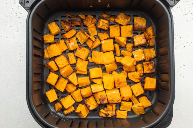 Overhead view of cubed butternut squash in an air fryer basket on a neutral countertop.