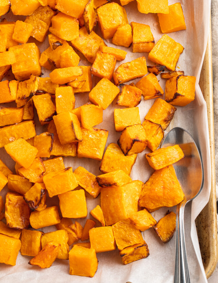 Overhead view of a sheet pan lined with parchment paper topped with cubed air fryer butternut squash.