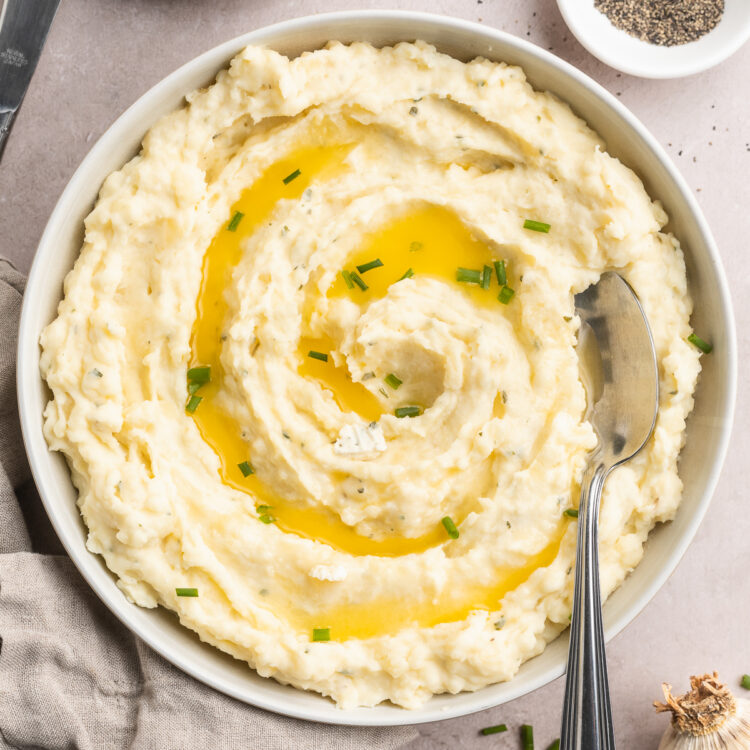 Overhead, zoomed out view of creamy boursin mashed potatoes in a large bowl. Potatoes are garnished with chives and melted butter.