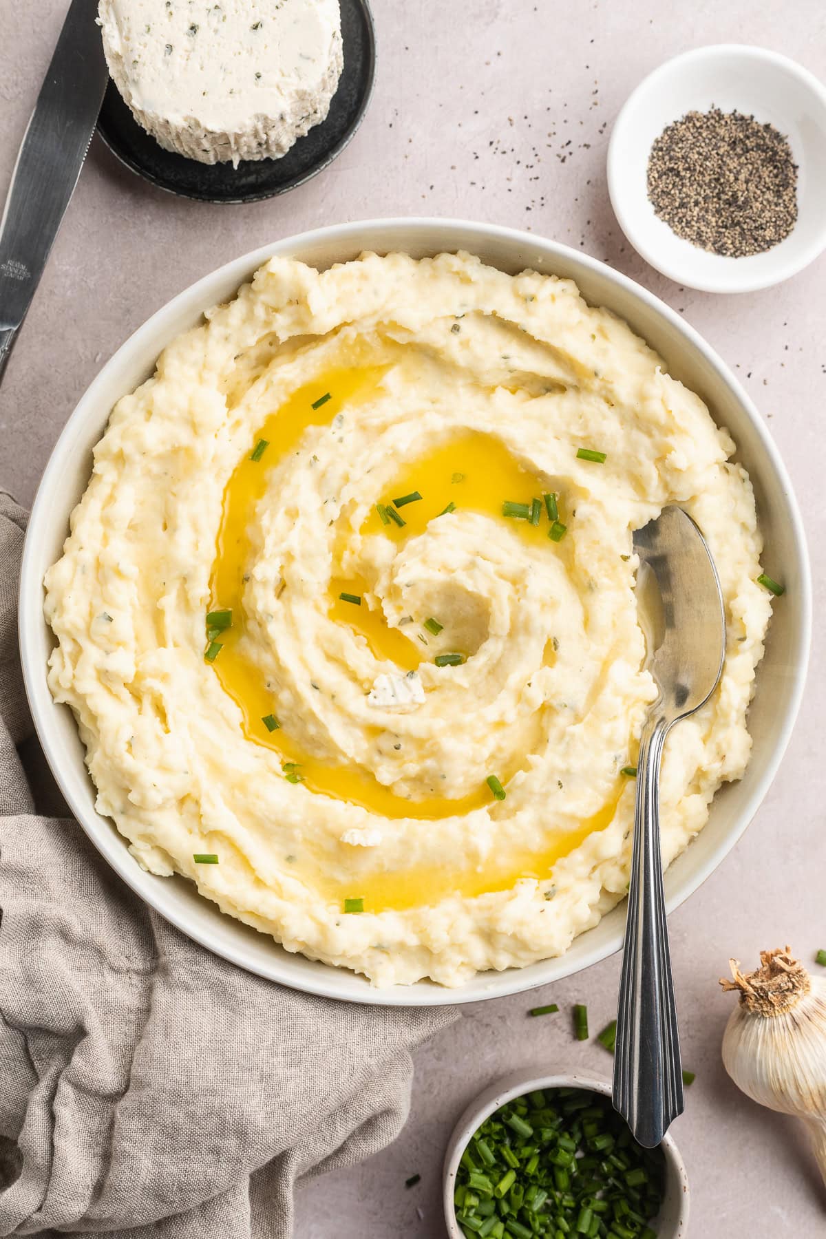 Overhead, zoomed out view of creamy boursin mashed potatoes in a large bowl. Potatoes are garnished with chives and melted butter.