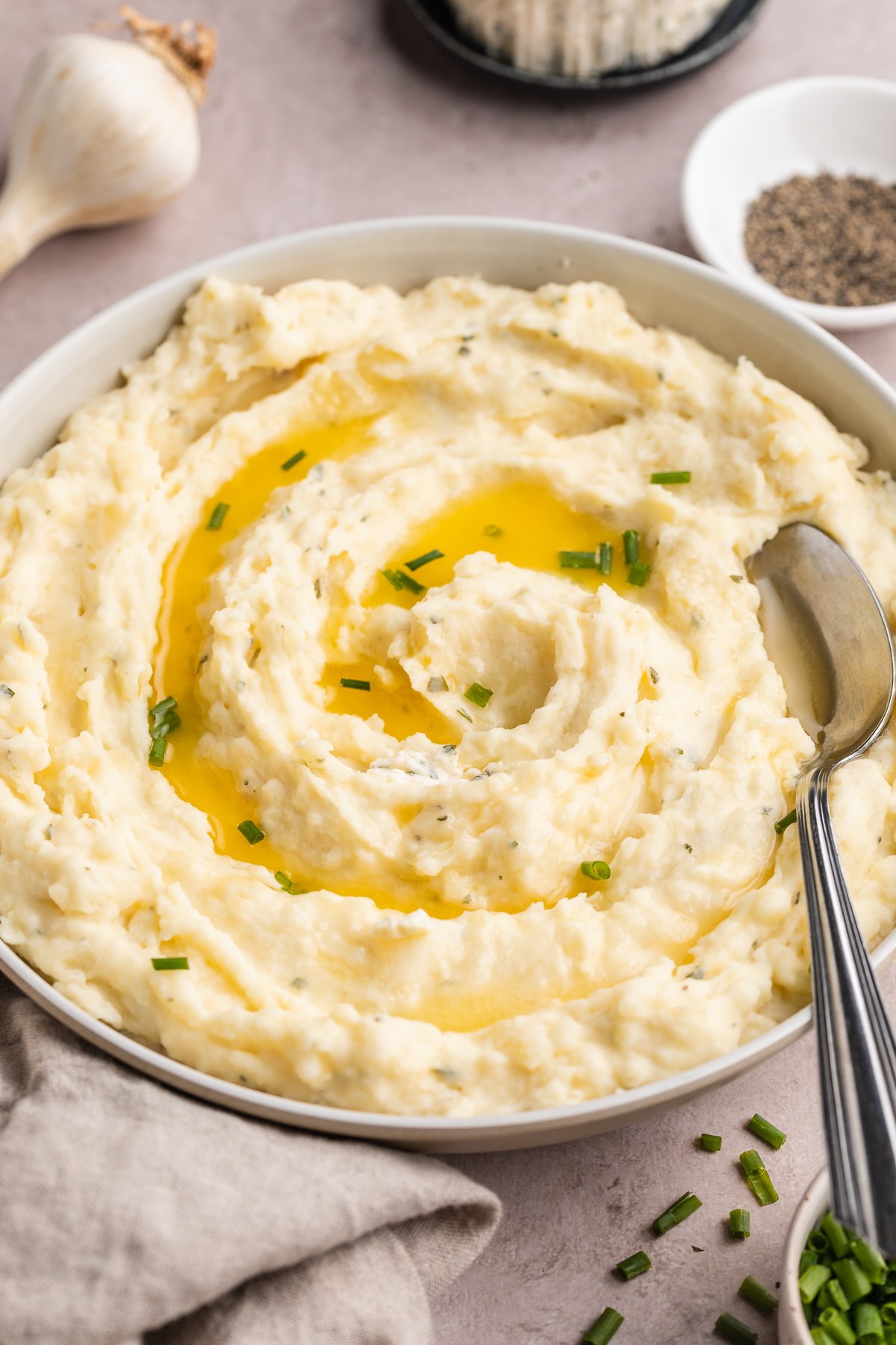 Angled overhead view of a big bowl of creamy Boursin mashed potatoes topped with melted butter and chopped chives.