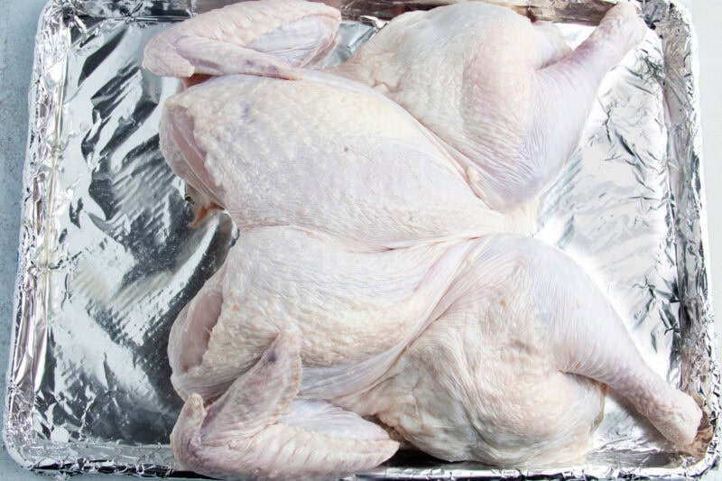 Overhead view of the breast-side of a spatchcocked turkey resting on a baking sheet wrapped in aluminum foil.